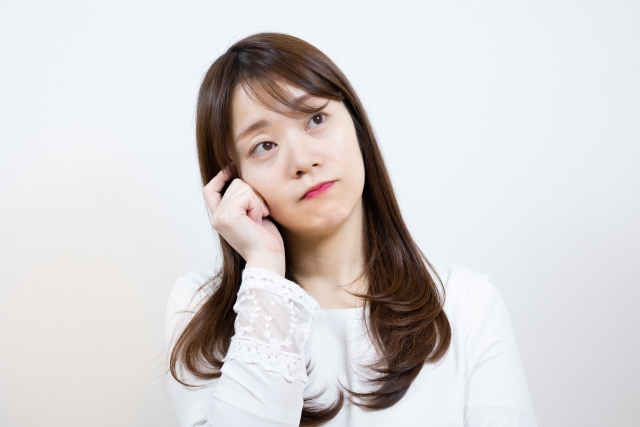 考え込む女性が頭に手を当て、遠くを見つめながら何かを思案している姿。彼女の目線が上方を向いており、深く考え込んでいる様子が伝わります。