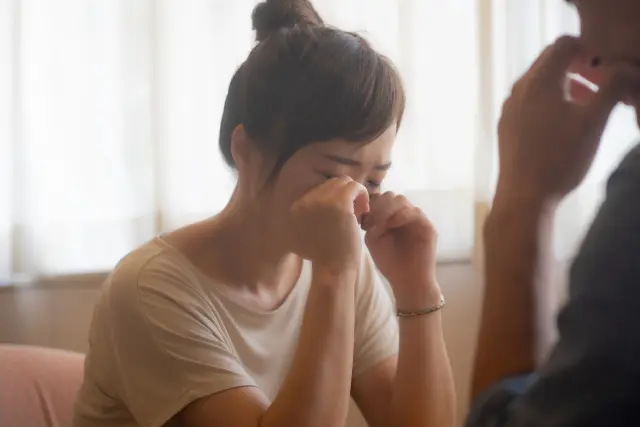感情的に傷ついた様子で目をこする女性のイメージ｜ストレスや自己イメージへの悩み、外見に対する不安を表現したシーン