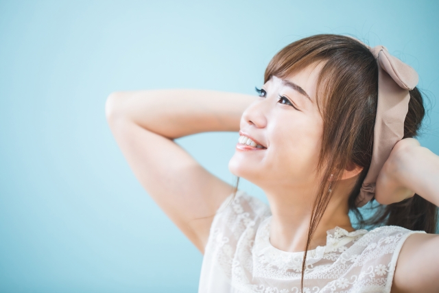頭の後ろで両手を組み、上を見上げながら笑顔を見せる女性。自宅での薄毛ケアやリラックスしたヘアケア時間をイメージさせるシーン。