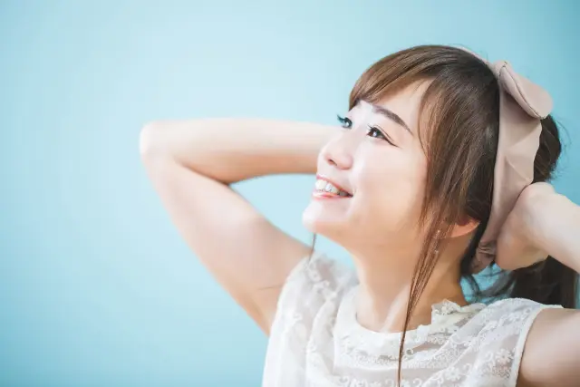 頭の後ろで両手を組み、上を見上げながら笑顔を見せる女性。自宅での薄毛ケアやリラックスしたヘアケア時間をイメージさせるシーン。