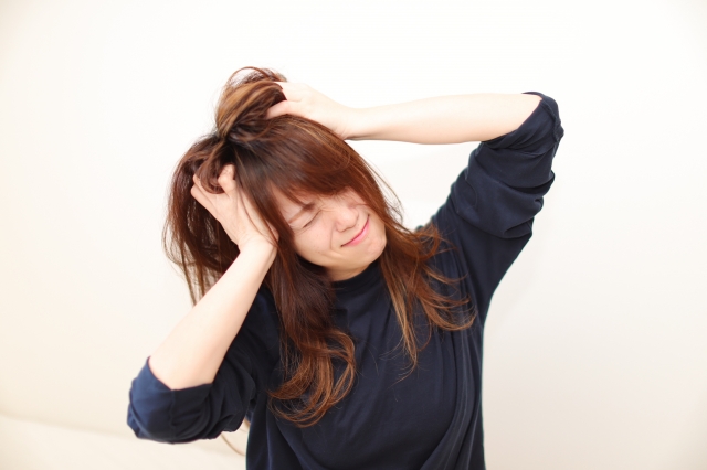 女性が頭を抱え、髪があちこちに広がっているシーン 髪の悩みやストレスを感じている女性の表情を表現した画像。髪が乱れ、広がる様子から、日常的な髪のトラブルや疲れを感じる瞬間を描いています。