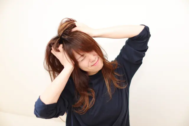 女性が頭を抱え、髪があちこちに広がっているシーン 髪の悩みやストレスを感じている女性の表情を表現した画像。髪が乱れ、広がる様子から、日常的な髪のトラブルや疲れを感じる瞬間を描いています。