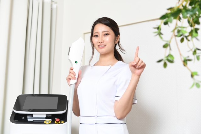 自宅でできる薄毛治療に使う機器を手に持ち、笑顔で説明する看護師。白く輝く歯を見せながら、もう一方の手で指を立ててポイントを示している様子。