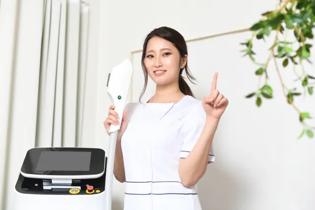 自宅でできる薄毛治療に使う機器を手に持ち、笑顔で説明する看護師。白く輝く歯を見せながら、もう一方の手で指を立ててポイントを示している様子。
