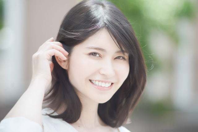 ツヤのある髪を右耳にかけながら微笑む日本人女性｜美髪ケア・ヘアスタイルの参考に最適