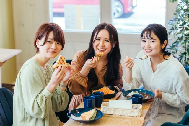 カフェのテーブルを囲んで笑顔でお茶を楽しむ女性たちのイメージ写真。リラックスした雰囲気の中で会話を楽しむ30代前後の女性3人。自毛植毛や外見の変化について自然に話し合う様子を連想させるシーン。