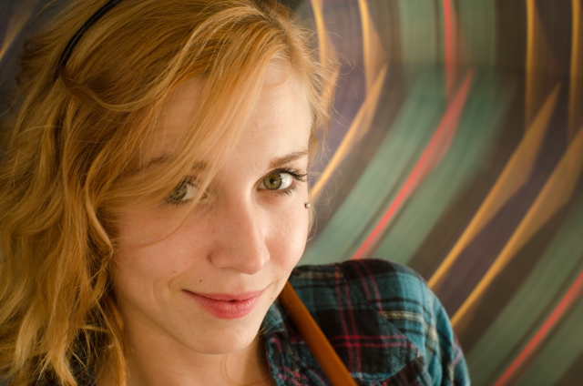 カメラを見つめて微笑むヨーロッパ系の女性。髪は亜麻色にオレンジがかすかに混ざり、まるでキツネの美しい尾のような輝きを放っている。