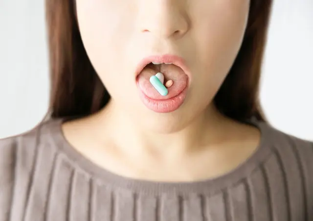 口を大きく開けてカラフルな錠剤を舌に乗せた女性のイメージ｜発毛治療薬や内服薬のイメージカットとして使用可能なストック写真