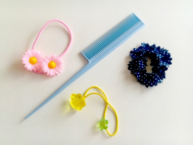 コーム（くし）と複数のヘアゴムが並べられた静物。アフリカ系女性の髪型を整える際に使われる日常的なヘアアイテムであり、髪型による毛根へのテンションや牽引性脱毛症（traction alopecia）との関連、適切なケア選択の重要性を象徴するビジュアル。