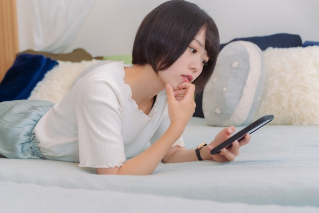 ベッドの上でスマートフォンを見ながら薄毛治療に関する最新コラムを読むボブヘアの若い女性。幹細胞やPRP療法など未来の毛髪再生医療に関心を寄せている様子を表現したイメージ。
