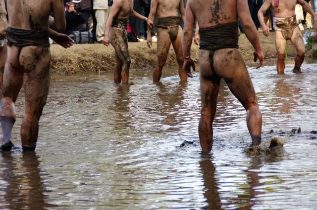 ふんどし姿の男性たちが泥の中を歩く、伝統的な日本の祭りの風景。自然の中で堂々とした姿を見せる彼らの様子は、薄毛や見た目にとらわれず、心身ともにたくましく生きる男性像を象徴し、若年性AGAとも向き合う勇気を暗示している。