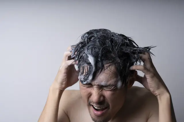 真剣な表情で両手を使い力強くシャンプーをする男性。ややコミカルな姿ながら、髪を守り育てようとする切実な思いがにじみ出ており、ポリフェノールなど自然由来の成分による毎日の頭皮ケアや育毛の重要性を表す場面。