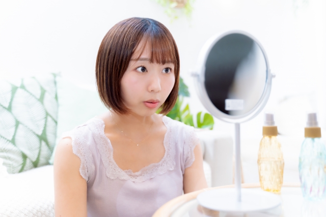 薄毛の進行に驚き、鏡を見つめる女性。生え際や頭頂部のボリューム低下に気づき、FUTやFUEによる自毛植毛を検討し始めた様子を象徴するストックイメージ。