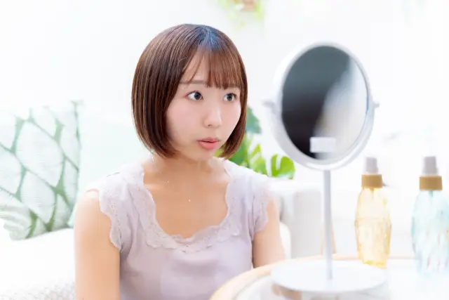 薄毛の進行に驚き、鏡を見つめる女性。生え際や頭頂部のボリューム低下に気づき、FUTやFUEによる自毛植毛を検討し始めた様子を象徴するストックイメージ。