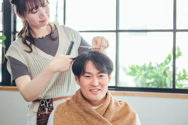 毛髪移植後に整った髪型で笑顔を見せる男性と、その髪を丁寧に整える美容師|自然な仕上がりに満足する様子を表現