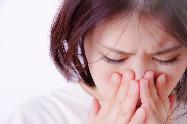 つわりによる吐き気に苦しむ妊娠中の女性の顔アップ写真。両手で口元を押さえ、産後脱毛やホルモンバランスの変化と深く関わる妊娠初期の体調変化を象徴している