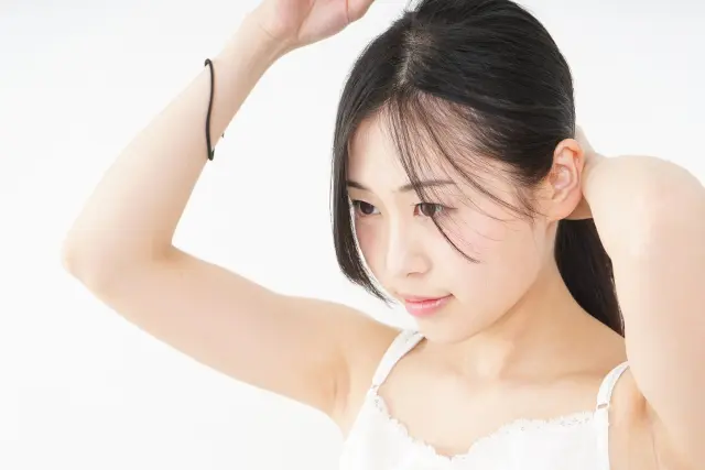 自然なツヤを放つ黒髪を結ぶ若い女性。白いタンクトップから覗く健康的で透明感のある美しい素肌が印象的。髪と肌の健康を象徴するビジュアルは、ポリフェノールによる自然派ケアの効果を視覚的に表現している。