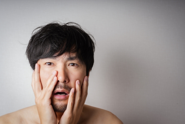 ヒゲのある日本人男性が両頬に手を添えて困惑した表情を浮かべる様子。ヒゲの薄さやデザインに悩む男性を象徴するイメージ。