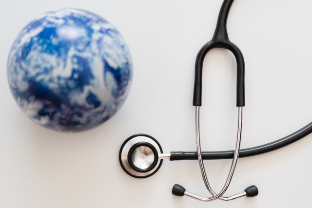 机の上に置かれた地球儀と聴診器の組み合わせが、国境を越えた医療ツーリズムやグローバル医療の広がりを象徴。世界中から治療先を選べる時代の到来をイメージした装飾的ビジュアル。