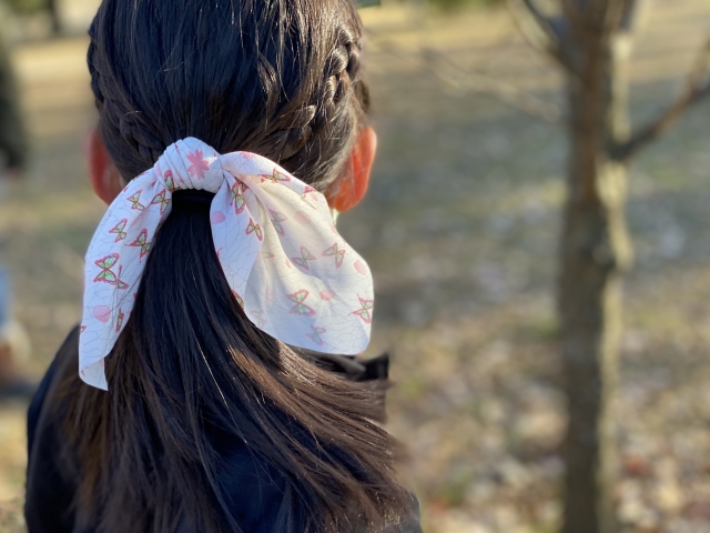 自然な髪の流れを表現したダークブラウンのポニーテールに、淡い花柄の大きなリボンが結ばれた後ろ姿。非外科的増毛法でも目指される、女性らしいナチュラルで美しいヘアスタイルの一例。