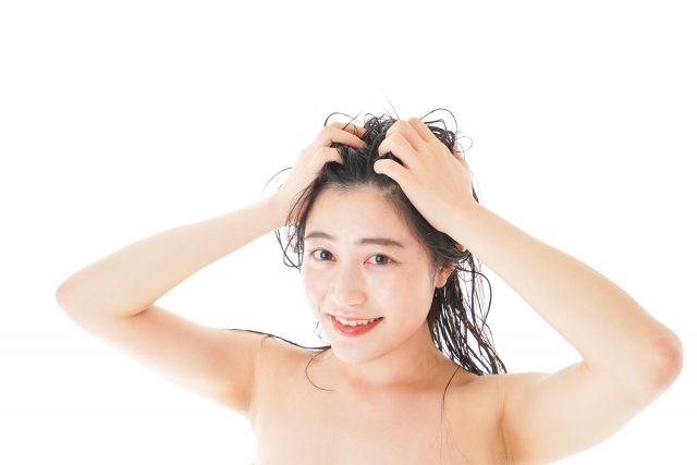 濡れた髪を両手で洗いながら笑顔を見せる女性。頭皮ケアや日常のヘアケア習慣が薄毛予防や毛髪再生治療の一環であることを示す象徴的なシーン｜薄毛対策と植毛手術に関する啓発記事用画像