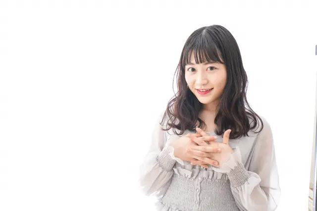 胸元に手を添えて微笑む女性のポートレート。顔まわりをやさしく縁取る自然な生え際と、鎖骨にかかるカールヘアが、清潔感と女性らしい魅力を演出するイメージ。ヘアラインの印象が第一印象に与える影響を表現。