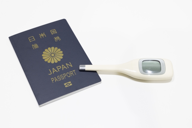 日本のパスポートと電子体温計が並ぶ様子は、海外での医療ツーリズムや自由診療を目的とした渡航を象徴。日本人が健康管理のために海外医療を選ぶ現代的な傾向を示すイメージ。