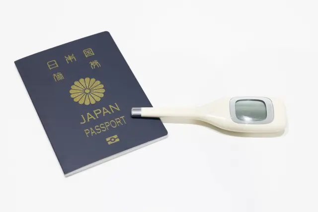 日本のパスポートと電子体温計が並ぶ様子は、海外での医療ツーリズムや自由診療を目的とした渡航を象徴。日本人が健康管理のために海外医療を選ぶ現代的な傾向を示すイメージ。