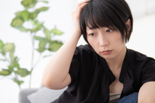 薄毛や外見の変化に悩む若い日本人女性がうつむき加減で考え込む様子。女性特有のびまん性脱毛や分け目の悩みに対し、自毛植毛や美容医療が注目される背景を象徴するイメージ写真