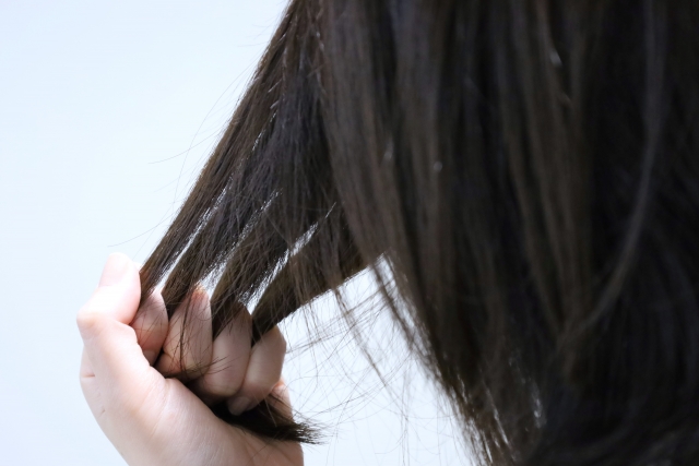 指の間で束ねられた髪がやさしく引き伸ばされている様子。髪の弾性や繊維構造、静電気や摩擦による影響を視覚的に示すシーン。ヘアケアの効果やキューティクル保護の重要性を象徴するイメージ。