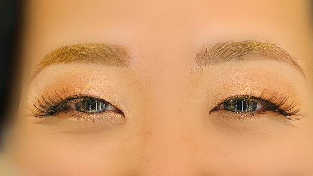 アイメイクが濃い女性の目元のクローズアップ。長くボリュームのある人工まつ毛としっかりと描かれたアイラインが印象的で、化粧によるまつ毛の演出と、医療による自然なまつ毛再建との違いを想起させるビジュアル。