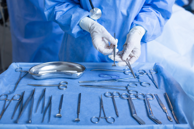 薄毛治療のために手術器具を準備する青い手術着の医師｜脱毛部位縮小術では薄毛部分の頭皮を外科的に切除する処置が行われる