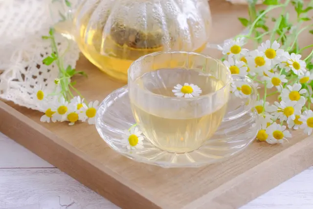 木製のトレイに美しく並べられたガラスのティーセットとカモミールティー。カップにはカモミールの花が浮かび、抗酸化作用を持つハーブの癒し効果や自然派育毛法における内側からのケアを象徴する一枚。薄毛対策やハーブ療法に関連するコラム記事の文脈に適した装飾写真。