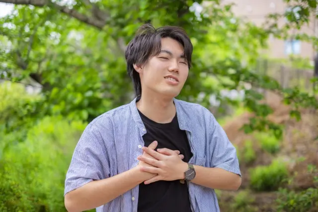軽度の肥満体型で髪の量が少ない若い男性が胸を押さえる様子。脱毛と心臓疾患や生活習慣病の早期兆候との関連性を示唆する場面。