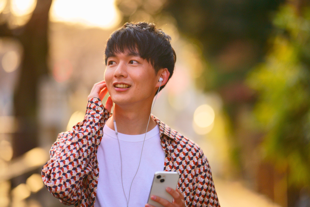 夕暮れ時の街を歩く大学生風の若年男性。耳元の髪を指でつまみ、薄毛が進行し始めた頭皮を気にするように複雑な表情を浮かべる。初期の脱毛に戸惑いながらも受け入れようとする心の揺れを表現。