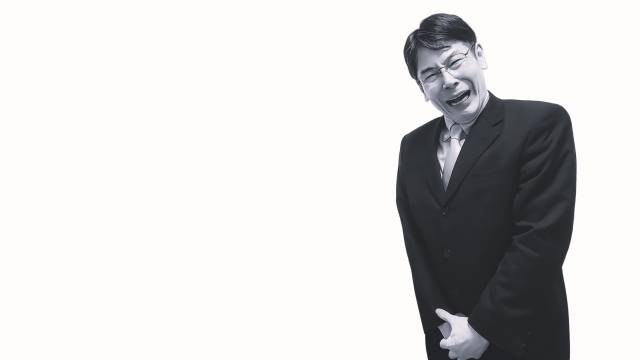 前立腺や下腹部の強い痛みに苦しむ中年男性の白黒写真。健康不安や体内の異常を訴える様子を象徴的に表現したイメージ。男性型脱毛症と前立腺がんの関連性に関する医療記事内の装飾用ビジュアル