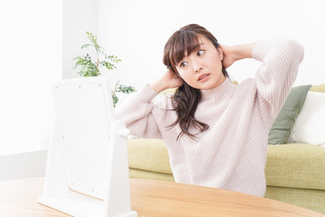 鏡の前で頭皮に異変を感じ、驚きと不安の表情を浮かべる女性。瘢痕性脱毛症に気づかず進行させてしまう恐れをイメージしたシーン