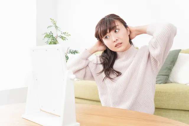 鏡の前で頭皮に異変を感じ、驚きと不安の表情を浮かべる女性。瘢痕性脱毛症に気づかず進行させてしまう恐れをイメージしたシーン