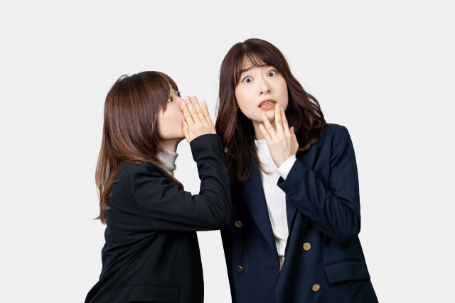 問診票に書きにくい喫煙や飲酒の情報を医師に正直に伝えるべきか迷っている様子を象徴する、女性同士の耳打ちと驚きのリアクション。自毛植毛前の健康申告の重要性を伝えるイメージとして使用