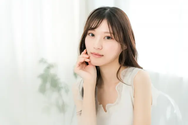 毛包再生による発毛治療の効果を実感するように、あごのラインをなぞる女性。ゆるやかにカールした長い髪が肩にかかり、健康的な髪の美しさと再生医療による薄毛対策の可能性を表現しているイメージ。