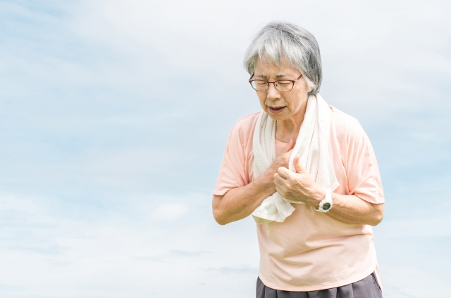 胸を押さえて呼吸の乱れと苦しさを訴える高齢女性の不安な表情を通じて、加齢に伴う薄毛や見た目の変化がもたらす身体的・心理的ストレスを象徴的に表現したイメージ｜脱毛縮小術による薄毛対策の啓発文脈で使用