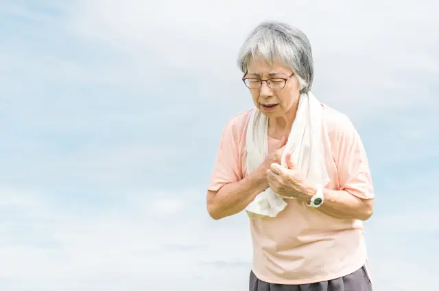 胸を押さえて呼吸の乱れと苦しさを訴える高齢女性の不安な表情を通じて、加齢に伴う薄毛や見た目の変化がもたらす身体的・心理的ストレスを象徴的に表現したイメージ｜脱毛縮小術による薄毛対策の啓発文脈で使用