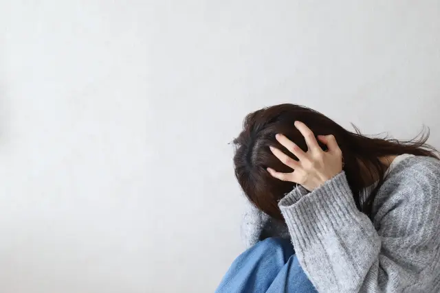 術後の痛みに対する不安から頭を抱える女性｜植毛手術は本当に痛いのかをテーマにしたコラム内のイメージカット