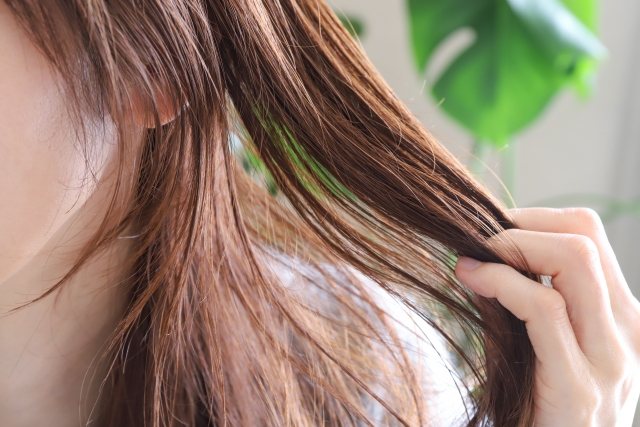 茶色い髪を手ぐしで整える人の横顔の一部｜脱毛後の毛髪再生を連想させる自然なヘアケア場面
