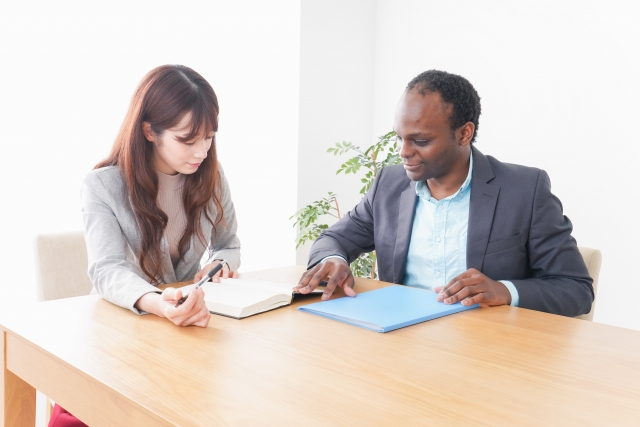 アフリカ系男性と日本人女性が書類を確認しながらカウンセリングを行う様子。自毛植毛の術前相談や治療方針の説明シーンをイメージした協調的な雰囲気のストック写真。