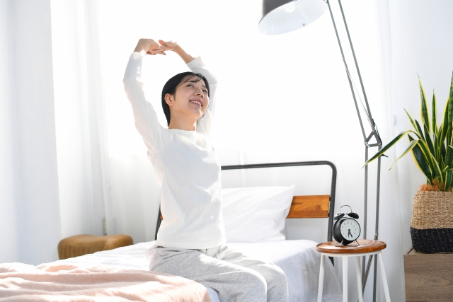 薄毛治療で前向きな毎日を取り戻しつつある女性が、朝の目覚めとともにベッドで気持ちよくストレッチする様子｜女性の髪の悩みと再生医療の情報コラム用イメージ