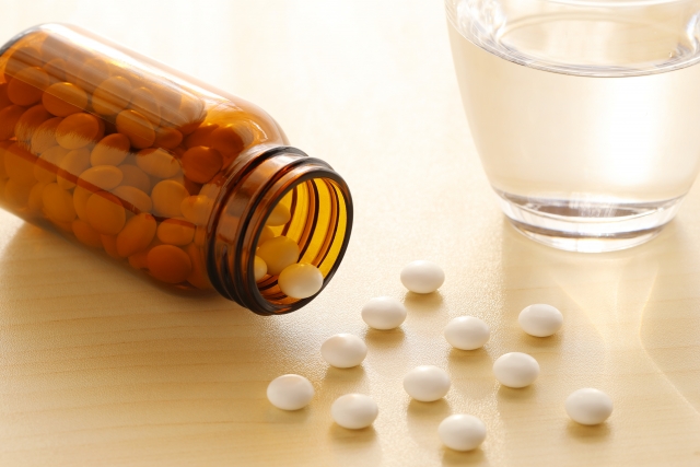 無造作に散らばった白い錠剤と茶色の薬瓶、透明な水の入ったコップ｜市販の育毛内服薬や自己判断による薄毛治療の象徴的イメージ