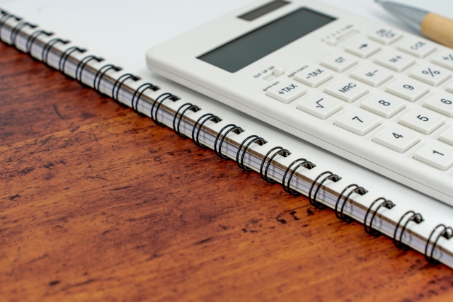 植毛の費用を比較・計算するための電卓とノートが置かれた木製デスクの風景
