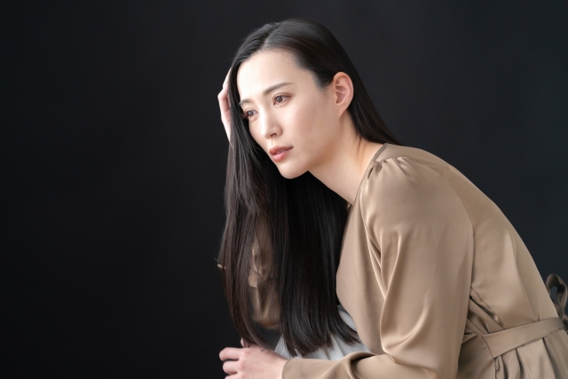 幹細胞による最先端の薄毛治療に希望を抱く中年の日本人女性が、長い髪を手ぐしで整えながら未来を見つめている様子。毛包再生やヘアクローニングの進歩により、女性の薄毛対策が新たな段階へと進んでいることを象徴するイメージ。