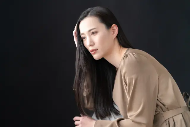 幹細胞による最先端の薄毛治療に希望を抱く中年の日本人女性が、長い髪を手ぐしで整えながら未来を見つめている様子。毛包再生やヘアクローニングの進歩により、女性の薄毛対策が新たな段階へと進んでいることを象徴するイメージ。